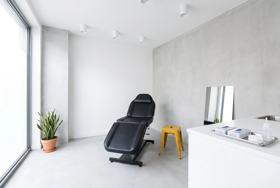 Sillón de tratamiento negro con una lámpara de luz cálida en un estudio en penumbra (imagen ilustrativa)