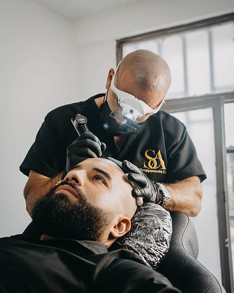 Santiago Abril con lupa de aumento iluminada y guantes negros, trabajando sobre la línea frontal de un paciente